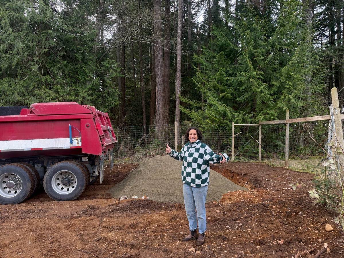 A volunteer giving a thumbs up beside a load of gravel delivered by dump truck
