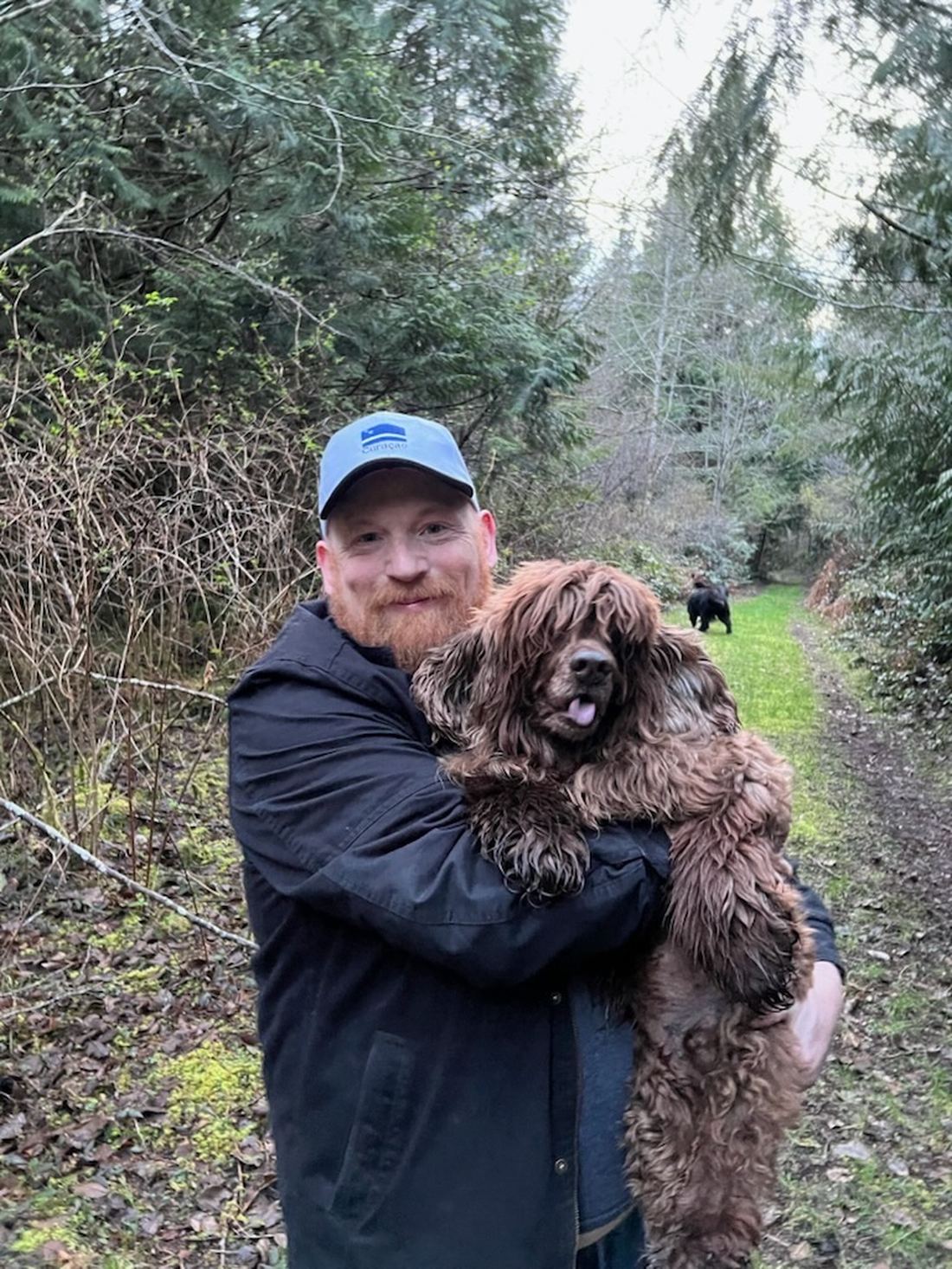 Keith Spinks carrying one of the sanctuary dogs along a forest trail on the property